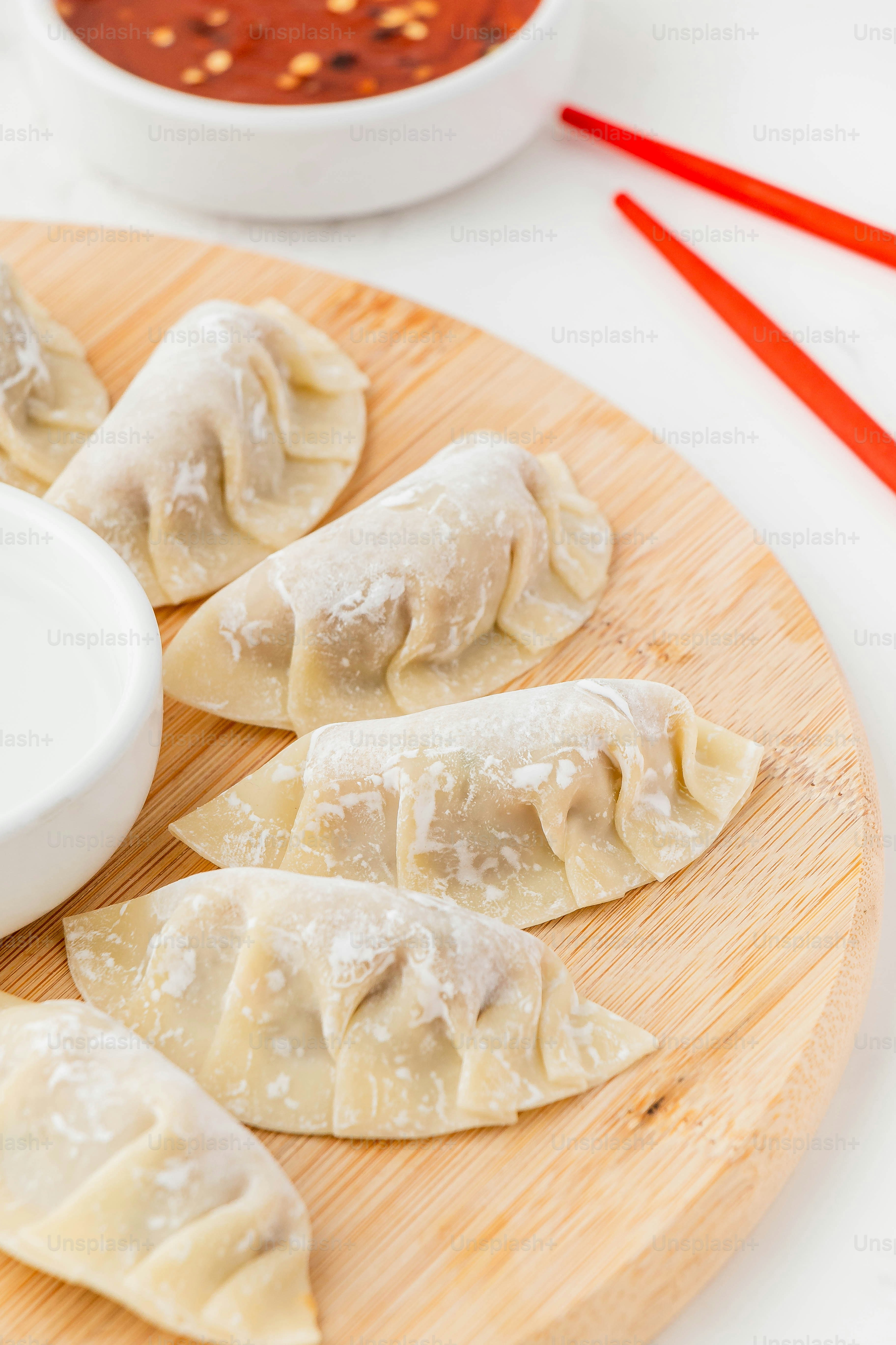 a wooden plate topped with dumplings next to a bowl of sauce
