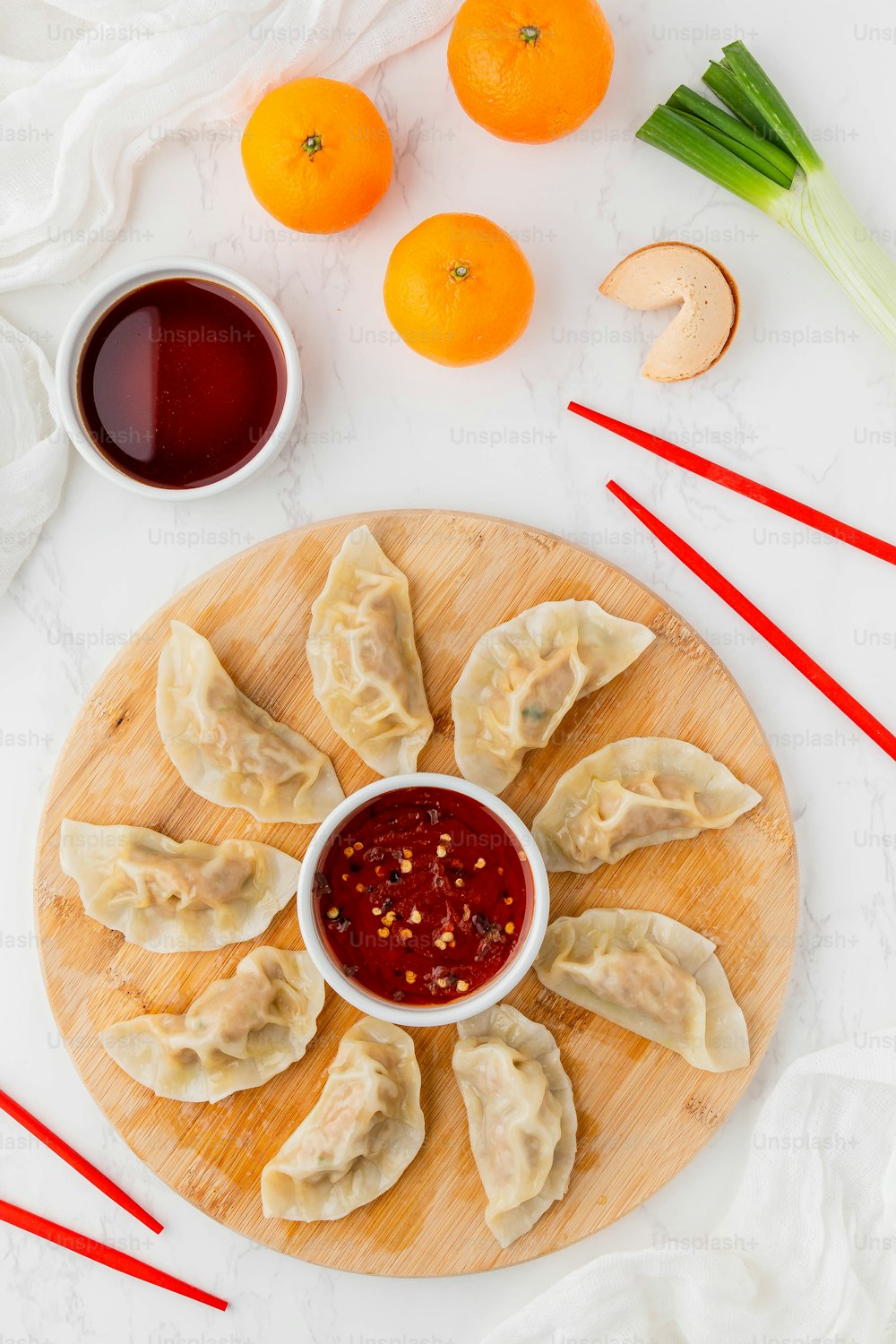 a plate of dumplings with dipping sauce next to oranges and chopsticks