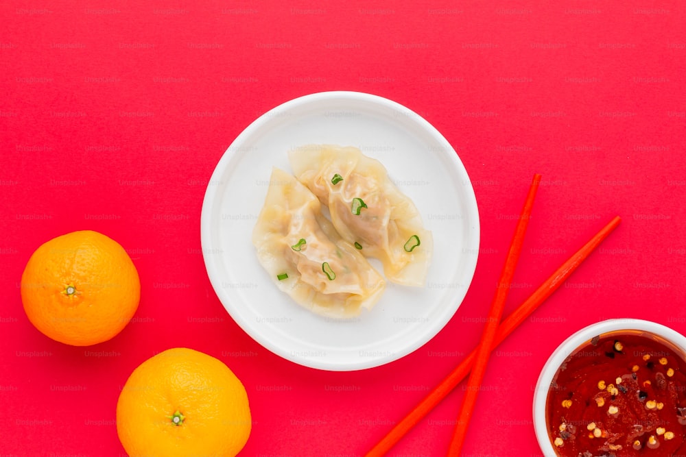 a bowl of dumplings and two oranges on a red surface