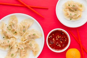 a plate of dumplings next to a bowl of sauce and chopsticks