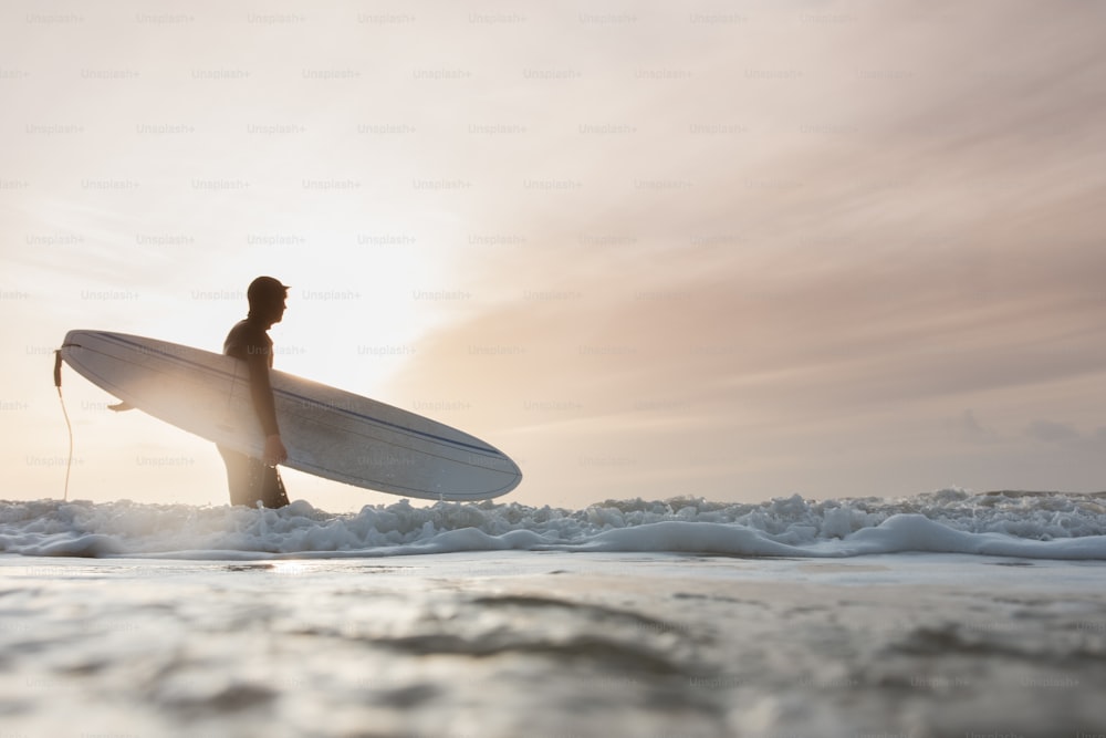 Un hombre sosteniendo una tabla de surf mientras está parado en el océano