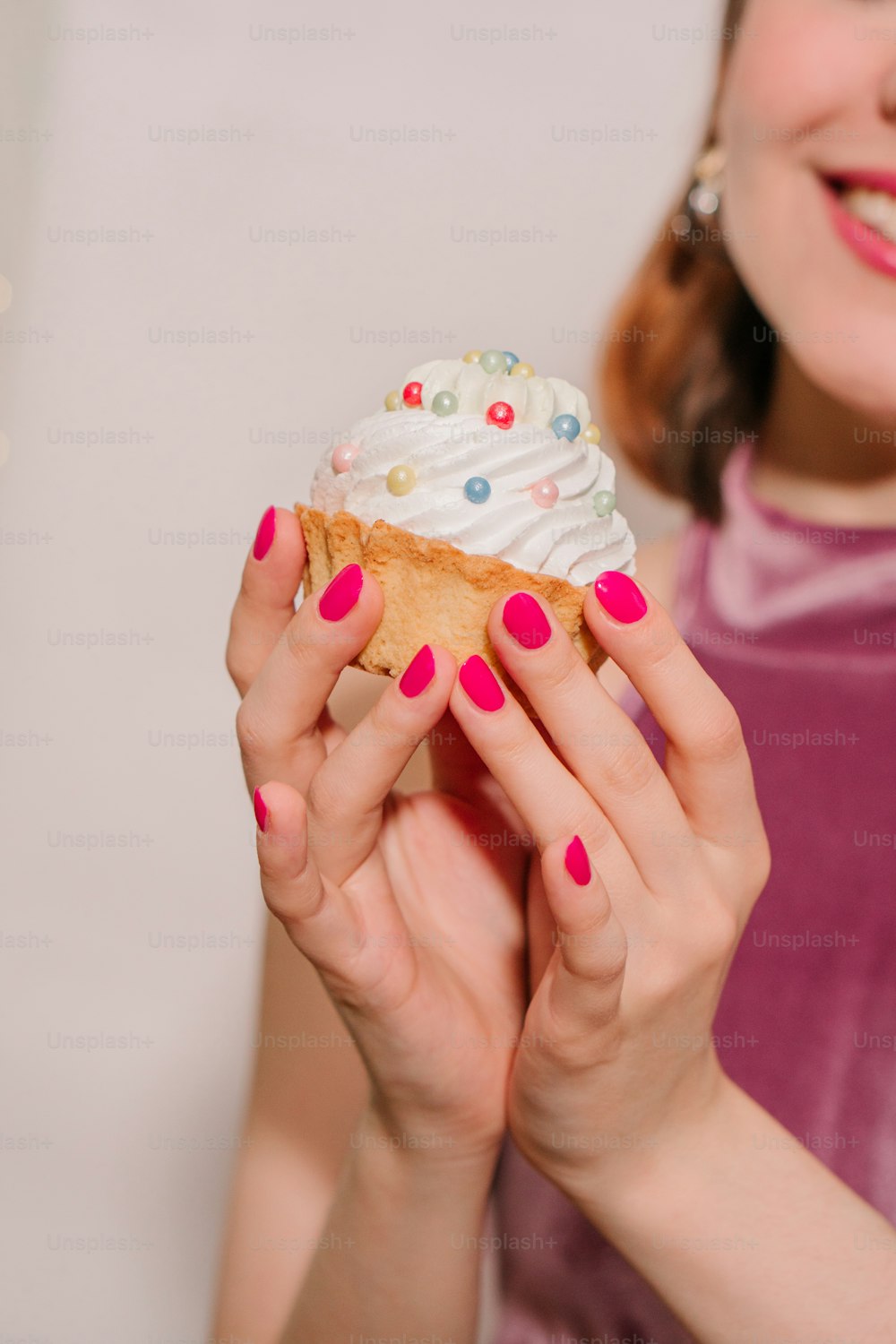 a woman holding a cupcake with white frosting and sprinkles