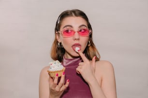 분홍색 안경을 쓴 여자가 컵케이크를 먹고 있다