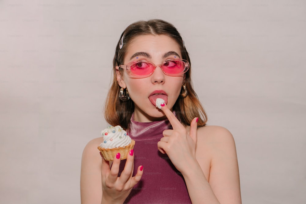 uma mulher que usa óculos cor-de-rosa está comendo um cupcake