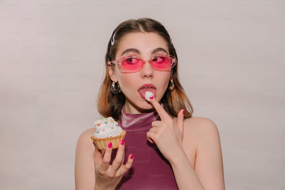 a woman wearing pink glasses is eating a cupcake