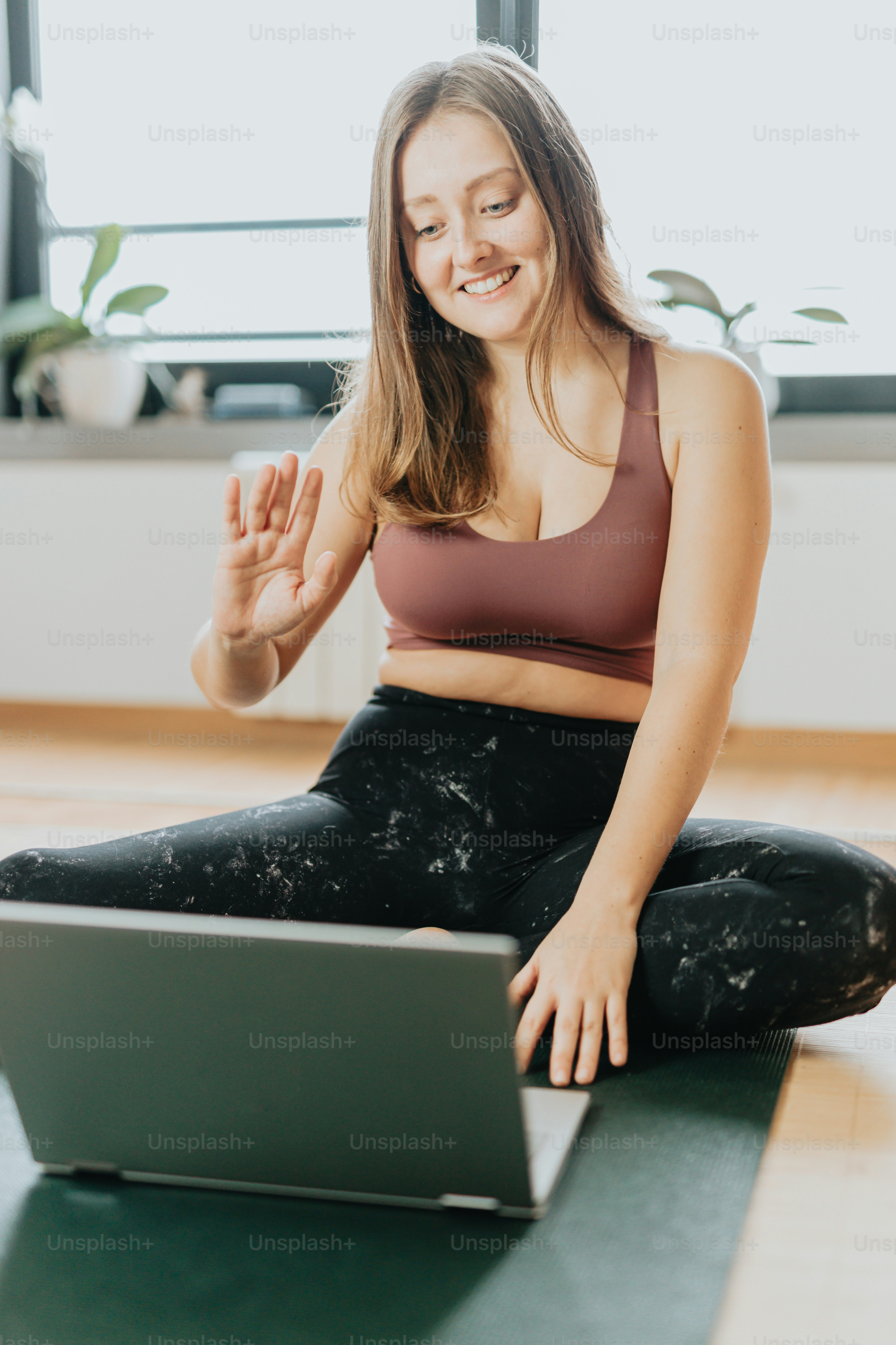a woman sitting on a yoga mat using a laptop
