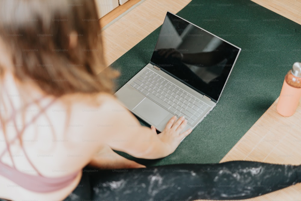 Una donna seduta su un tappetino da yoga usando un computer portatile