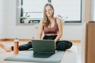 a woman sitting on a yoga mat using a laptop