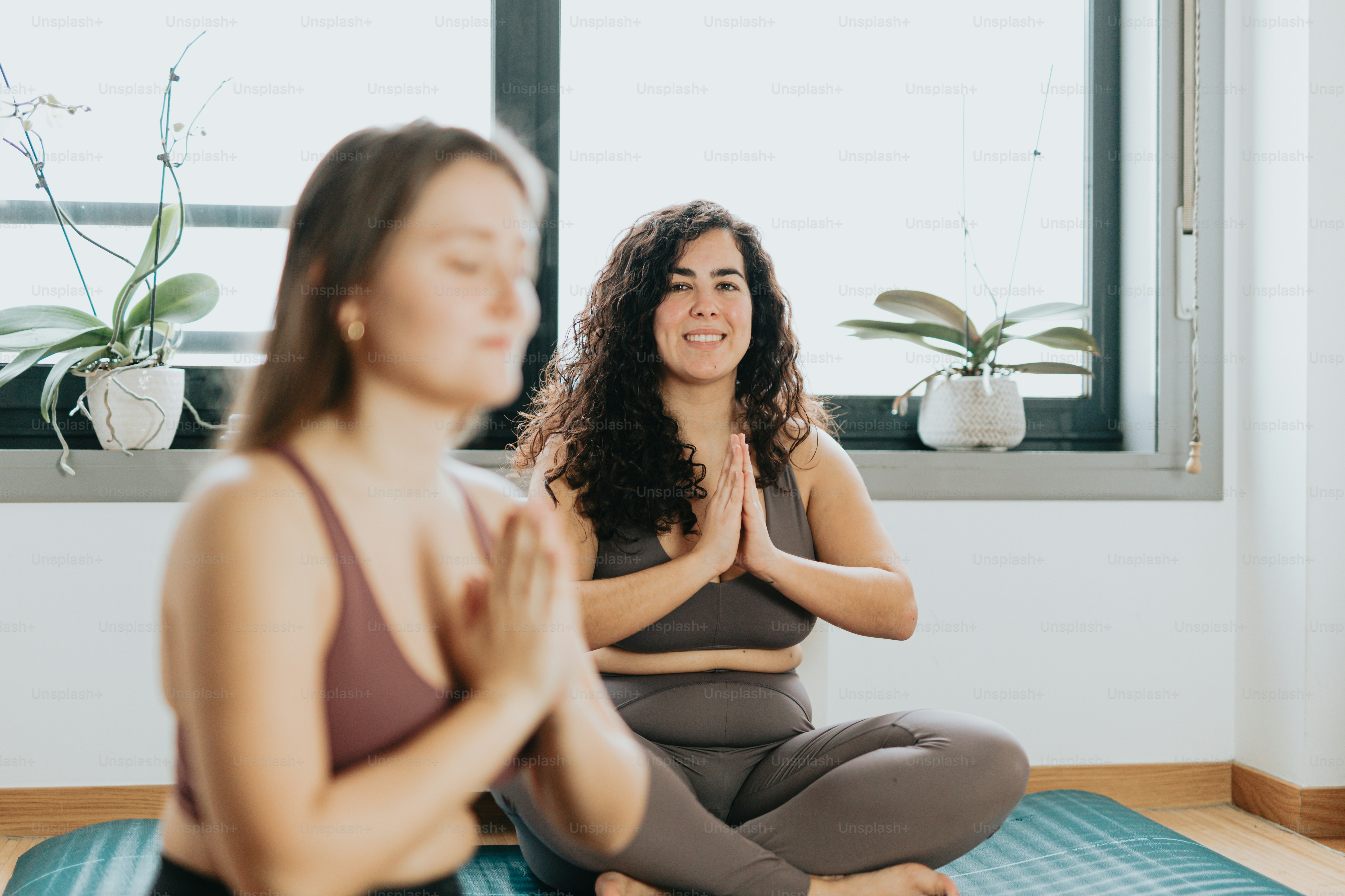two women sitting on yoga mats in front of a window