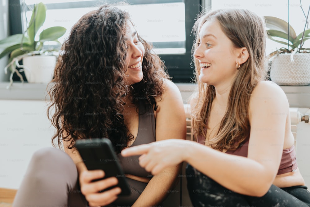 two women sitting next to each other looking at a cell phone