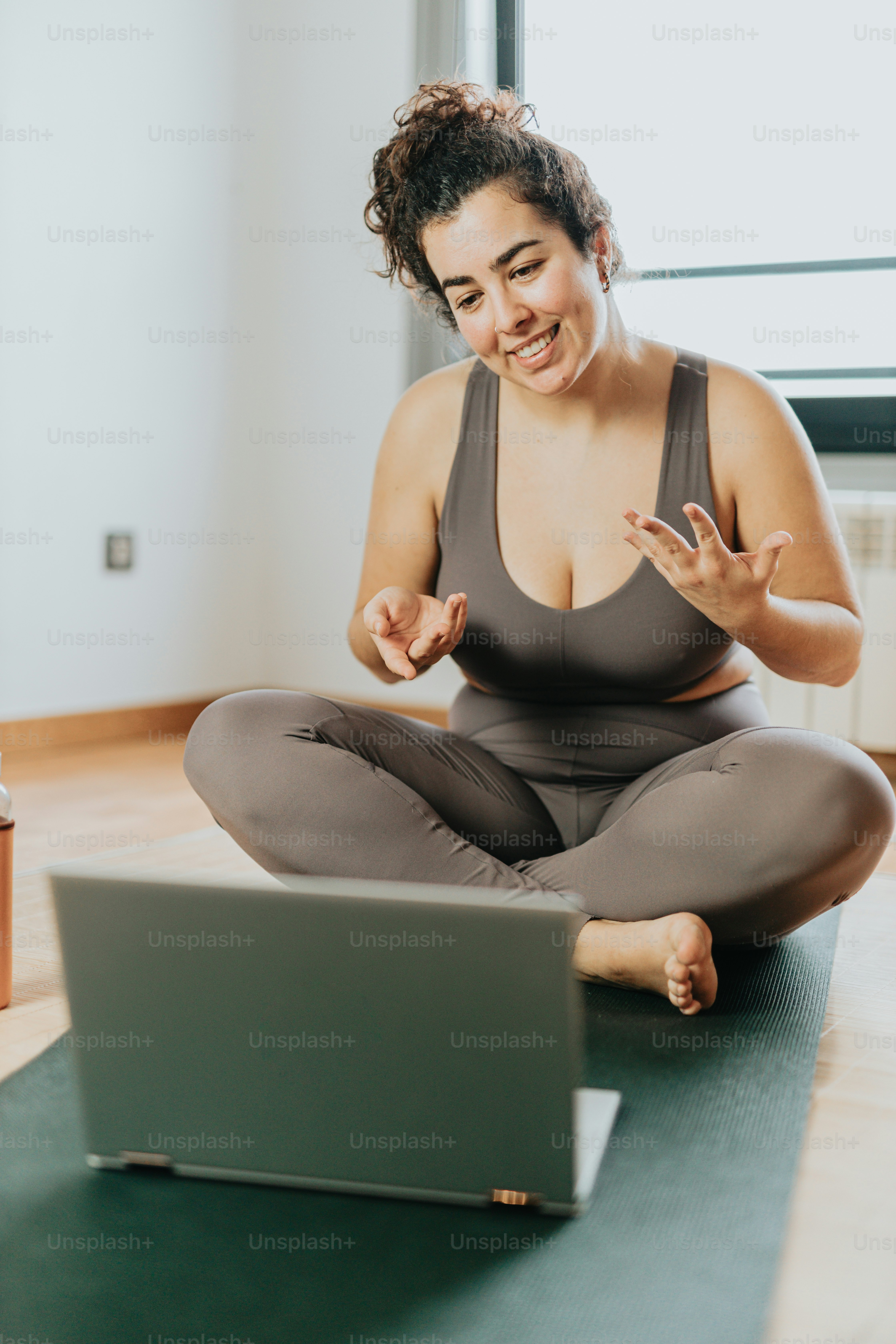 A woman sitting on a yoga mat in front of a laptop photo – Yoga Image ...
