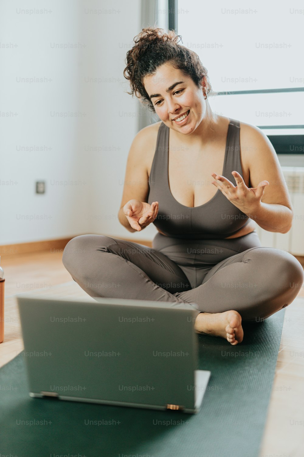 a woman sitting on a yoga mat in front of a laptop