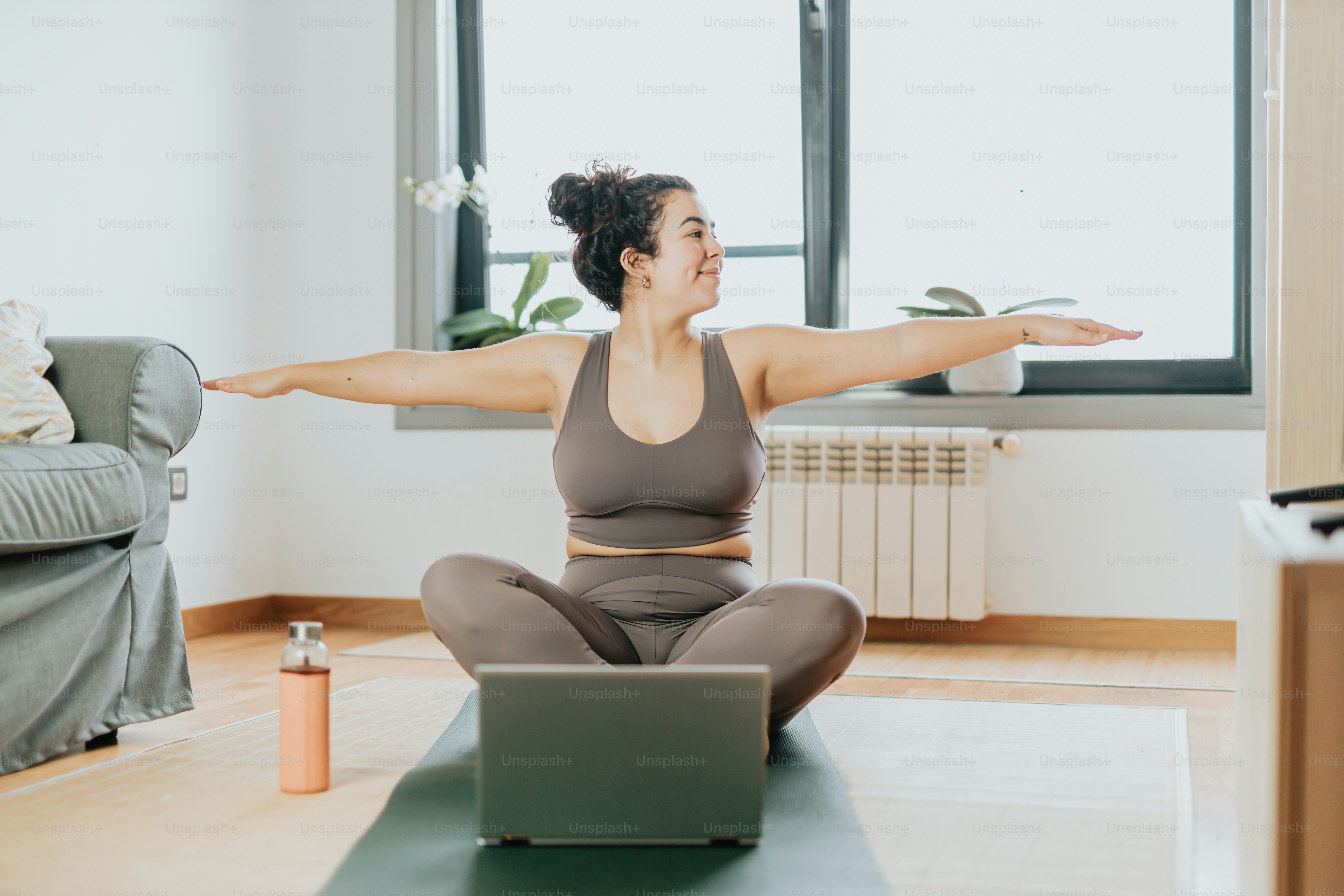 A woman sitting on a yoga mat with a laptop in front of her photo ...