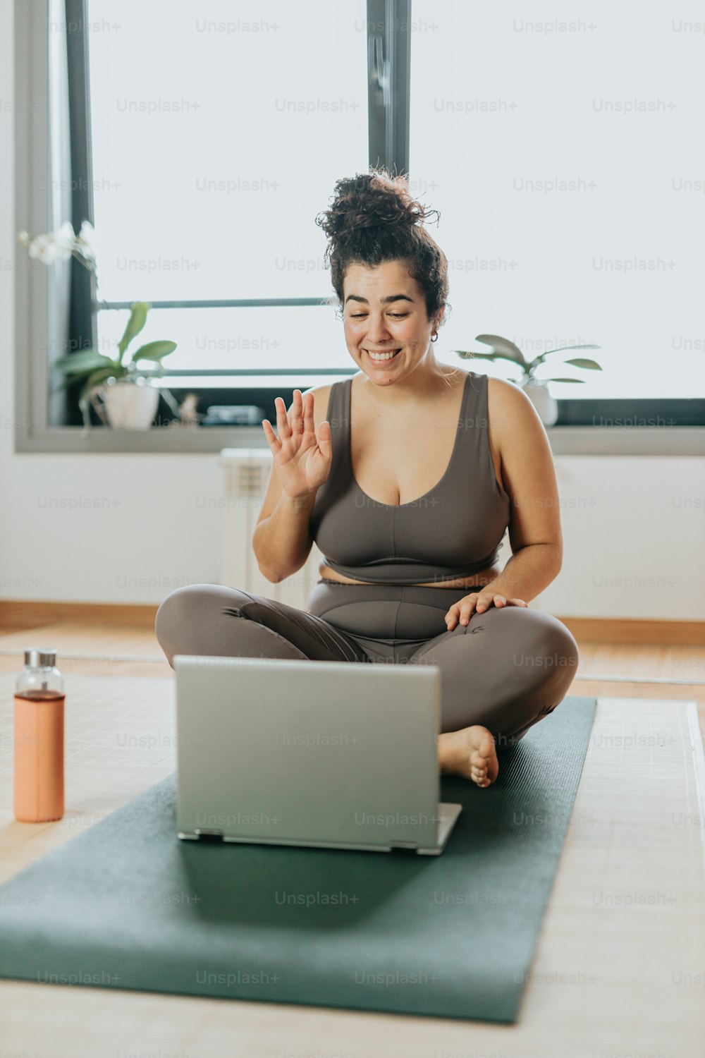 Una mujer sentada en una esterilla de yoga frente a una computadora portátil
