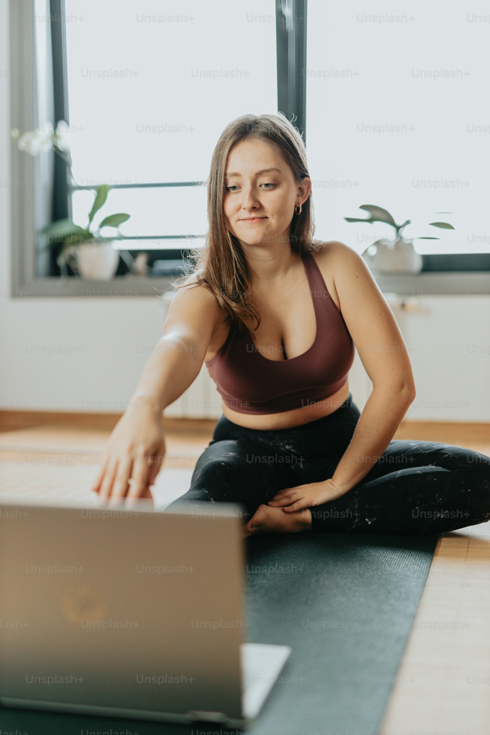 a woman sitting on a yoga mat in front of a laptop