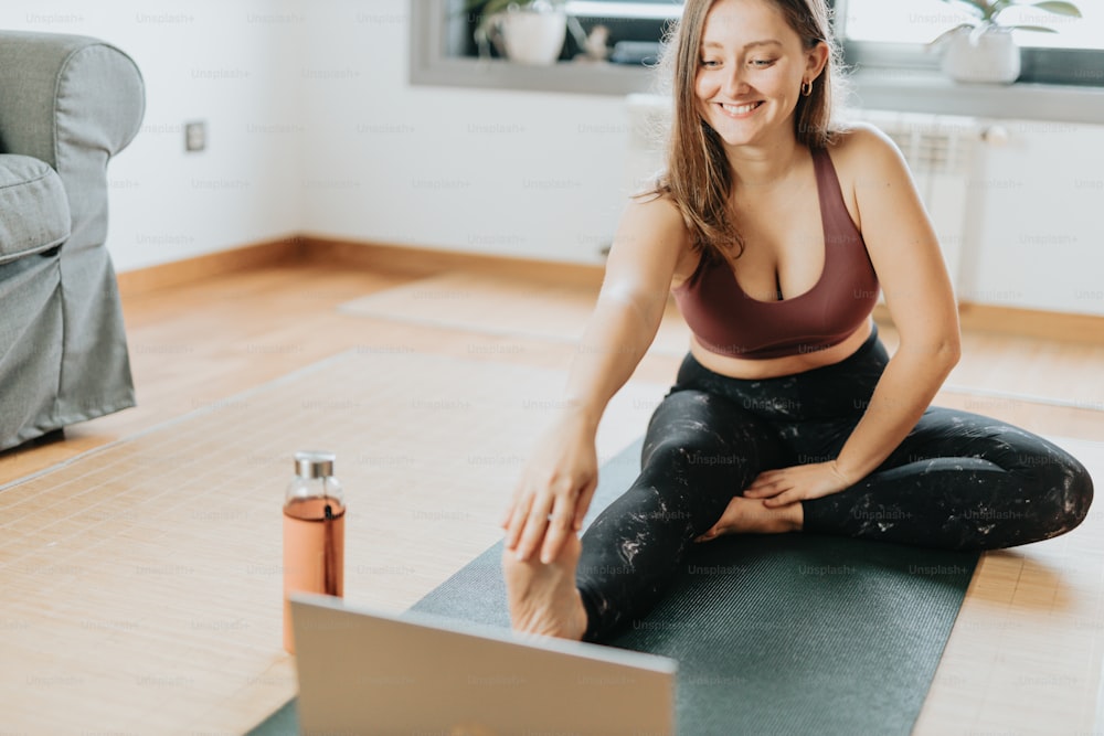 a woman sitting on a yoga mat using a laptop