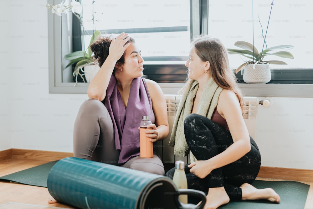 two women sitting on a yoga mat with a bottle of wine
