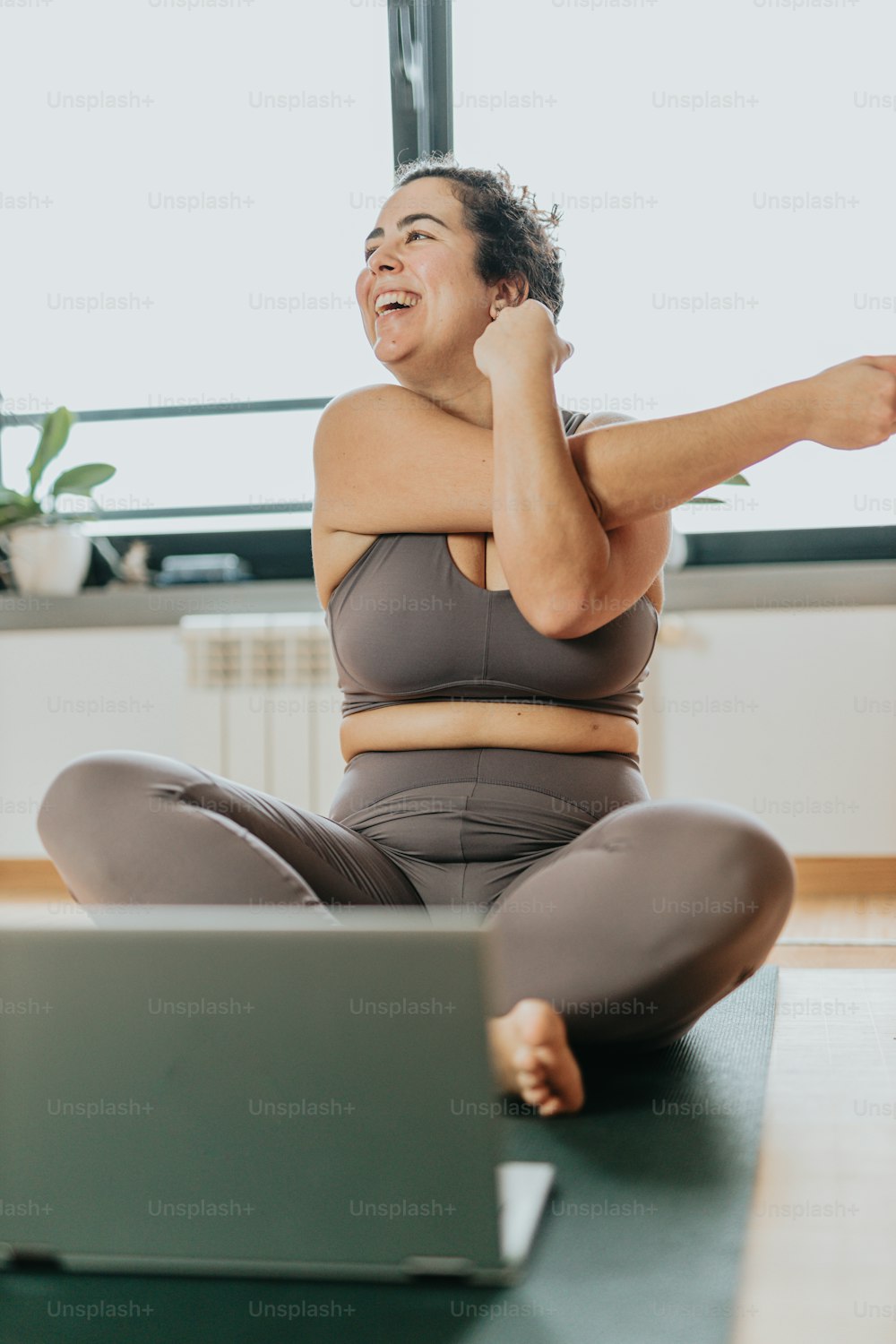 a woman sitting on a yoga mat with a laptop in front of her