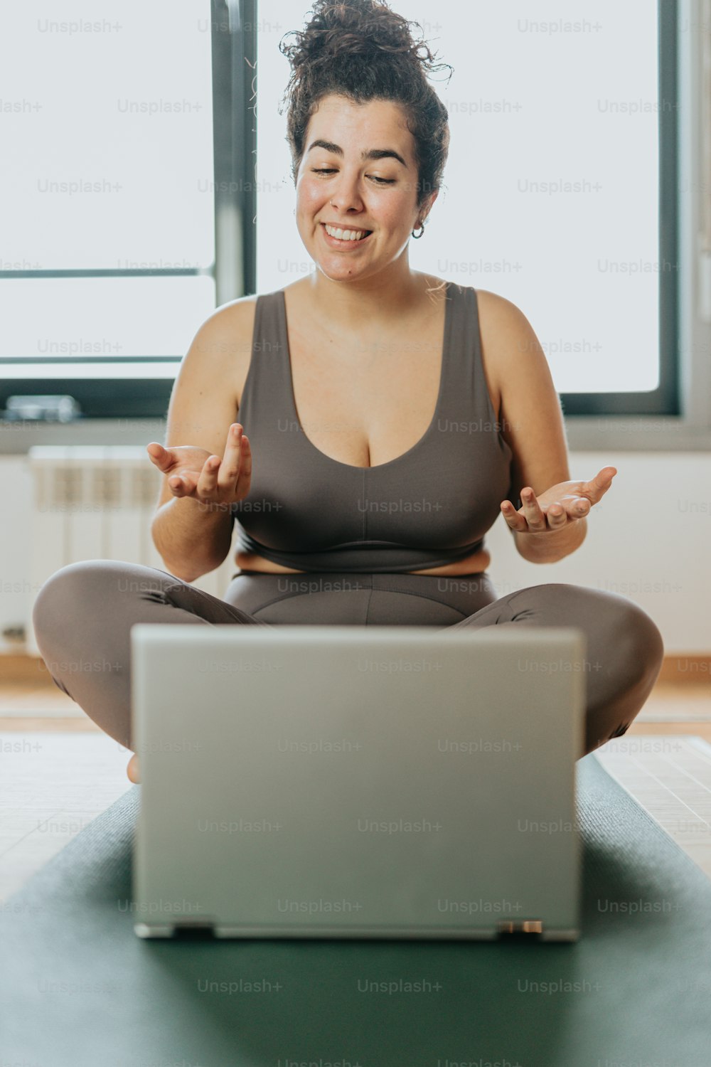 Una mujer sentada en una esterilla de yoga frente a una computadora portátil