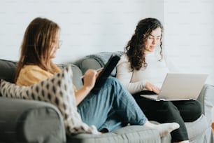 two women sitting on a couch looking at a laptop