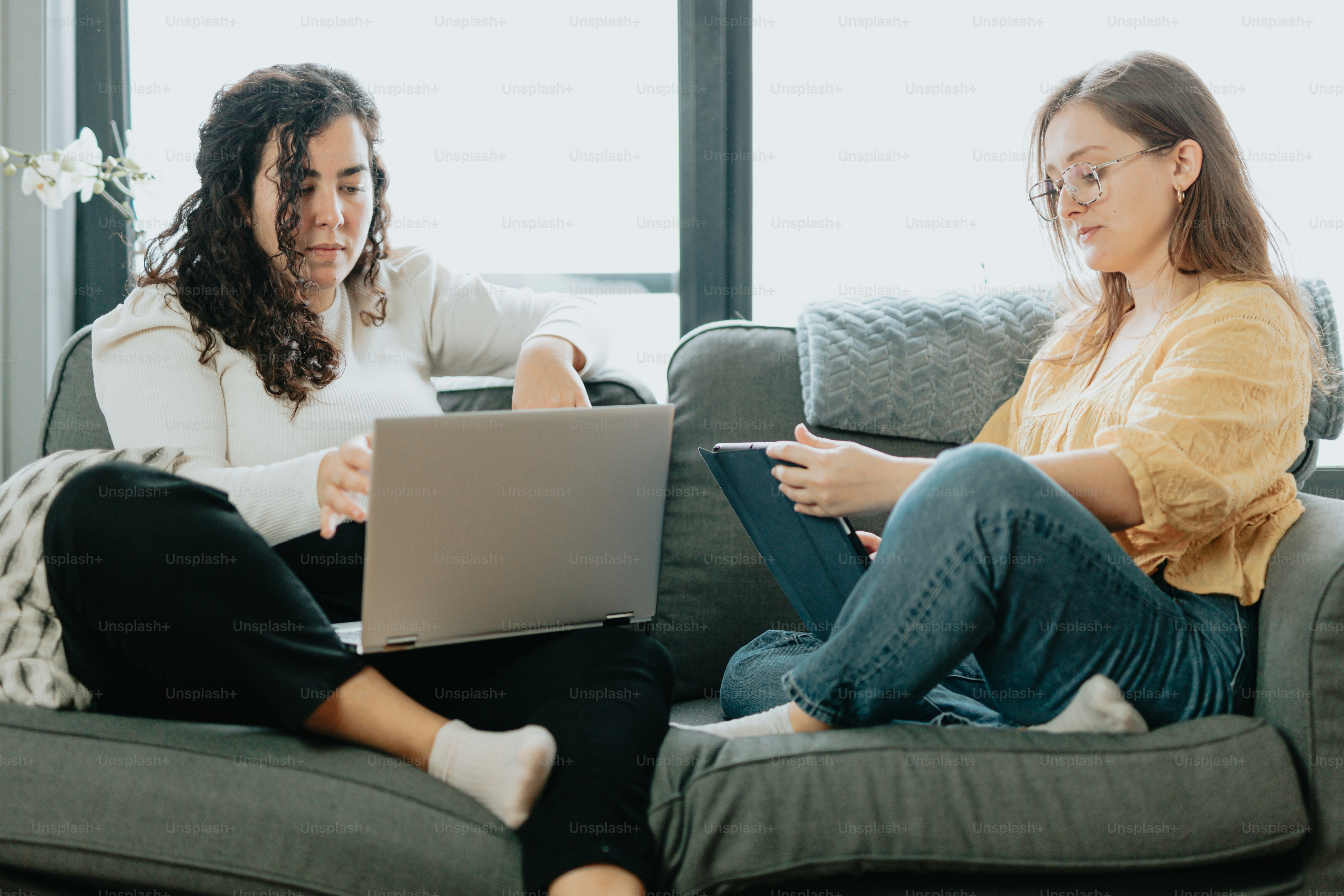two women sitting on a couch looking at a laptop