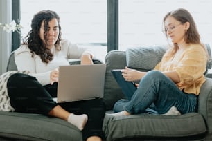 two women sitting on a couch looking at a laptop