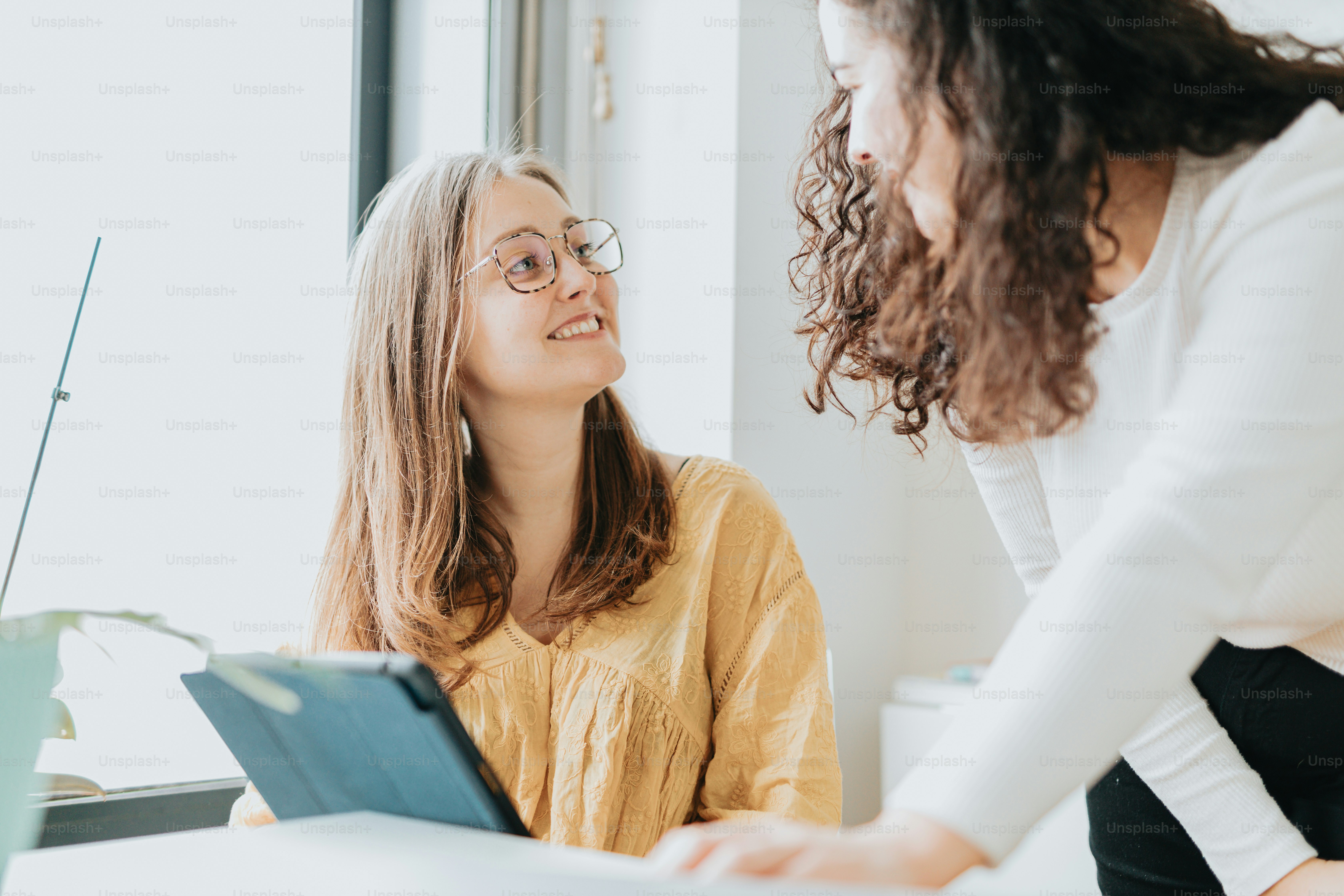 two women sitting at a table with a tablet