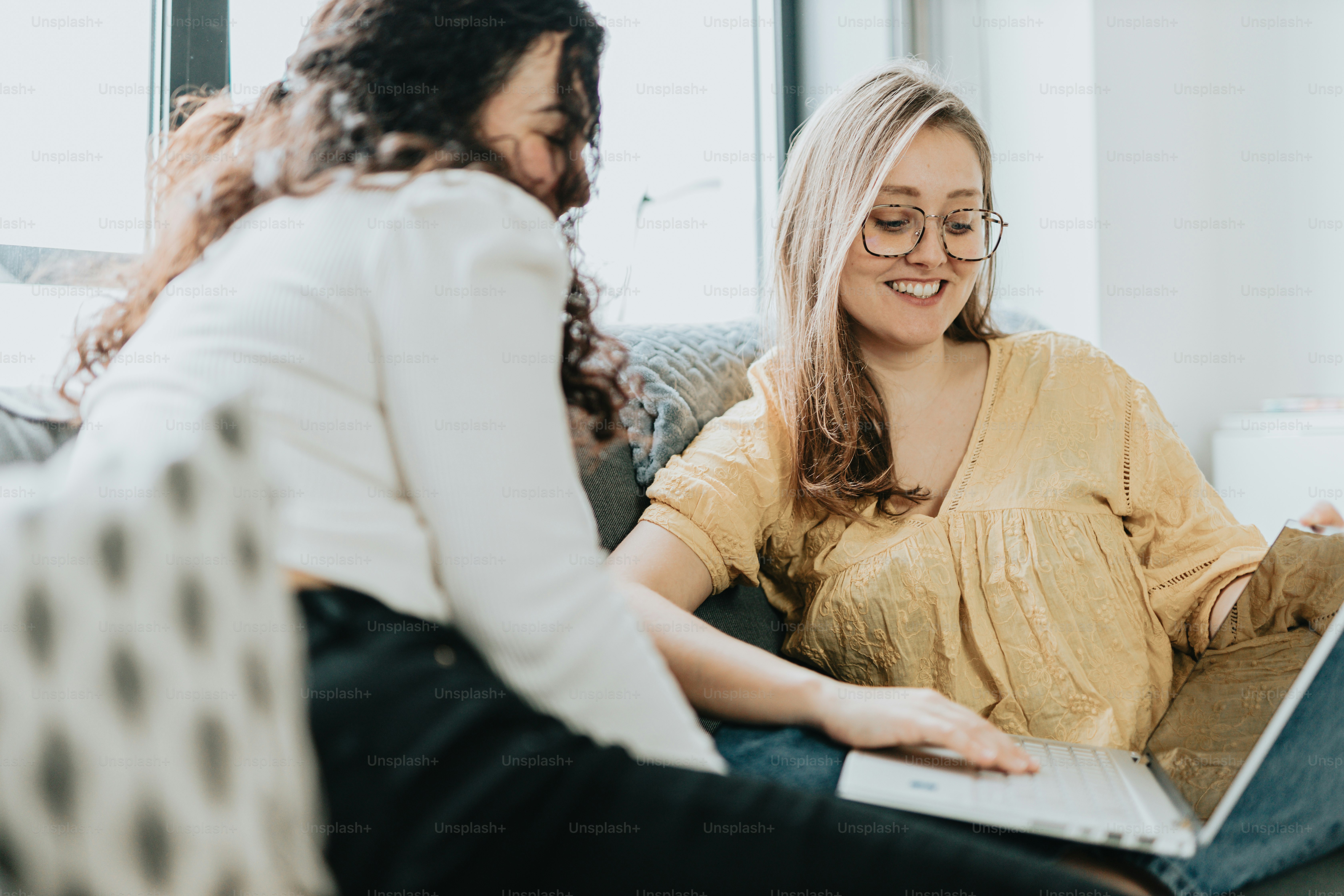 two women sitting on a couch looking at a laptop