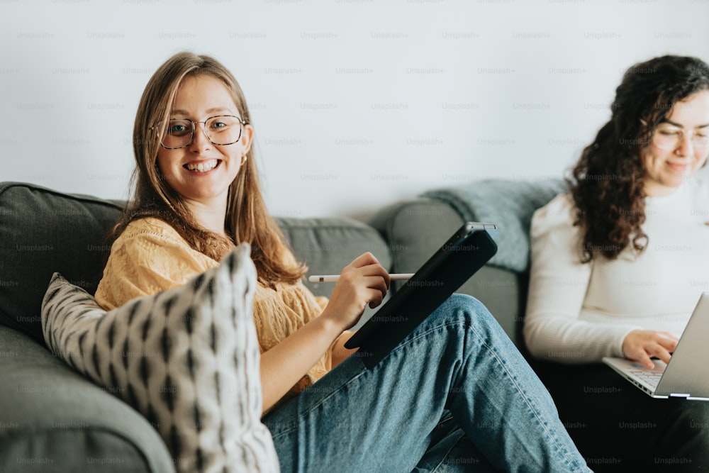 two women sitting on a couch with laptops