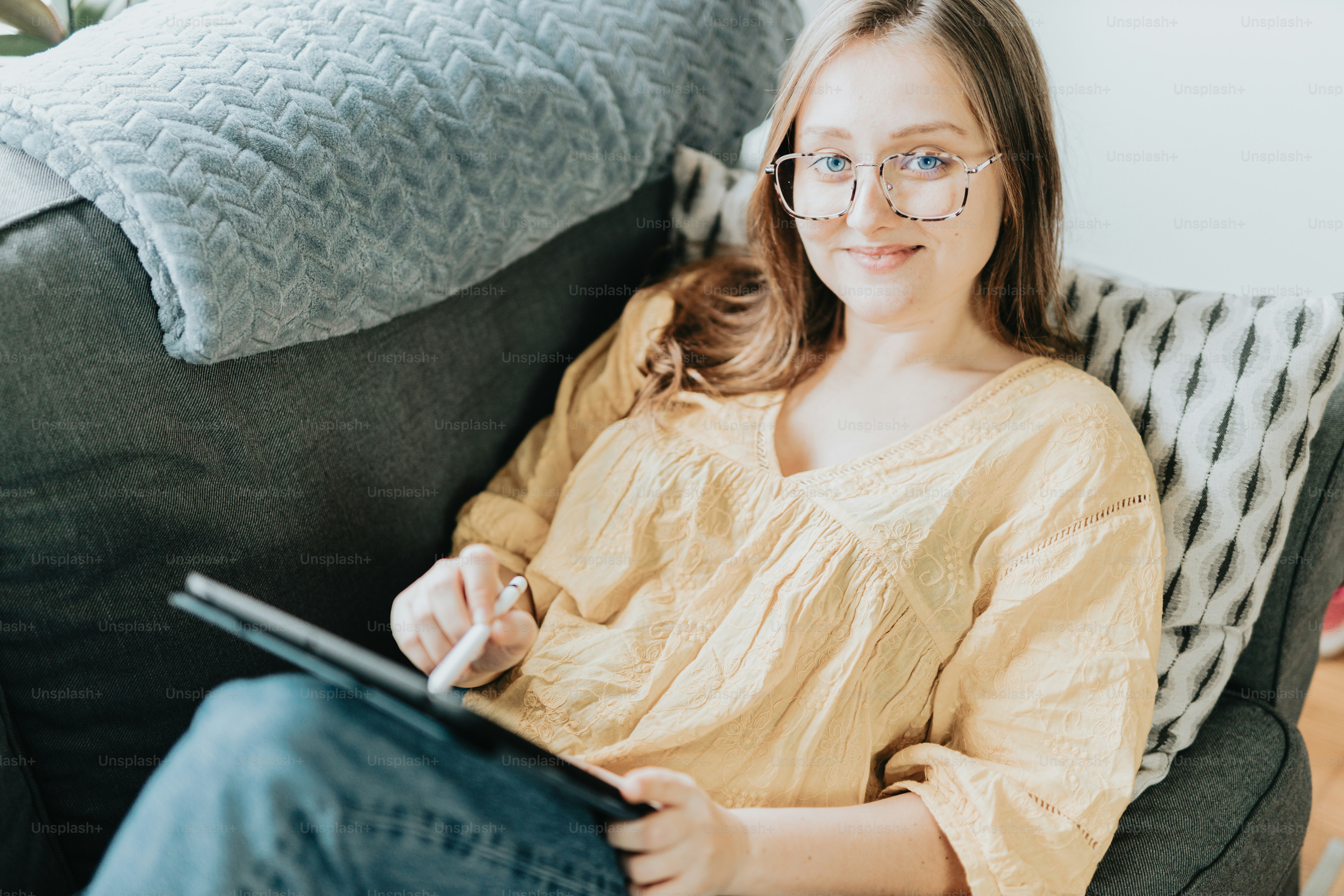 A woman sitting on a couch holding a tablet photo – Female Image on ...