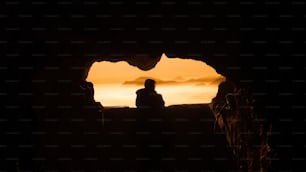 une personne debout dans une grotte regardant le coucher du soleil