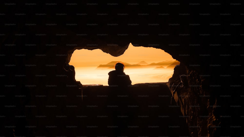 a person standing in a cave looking out at the sunset