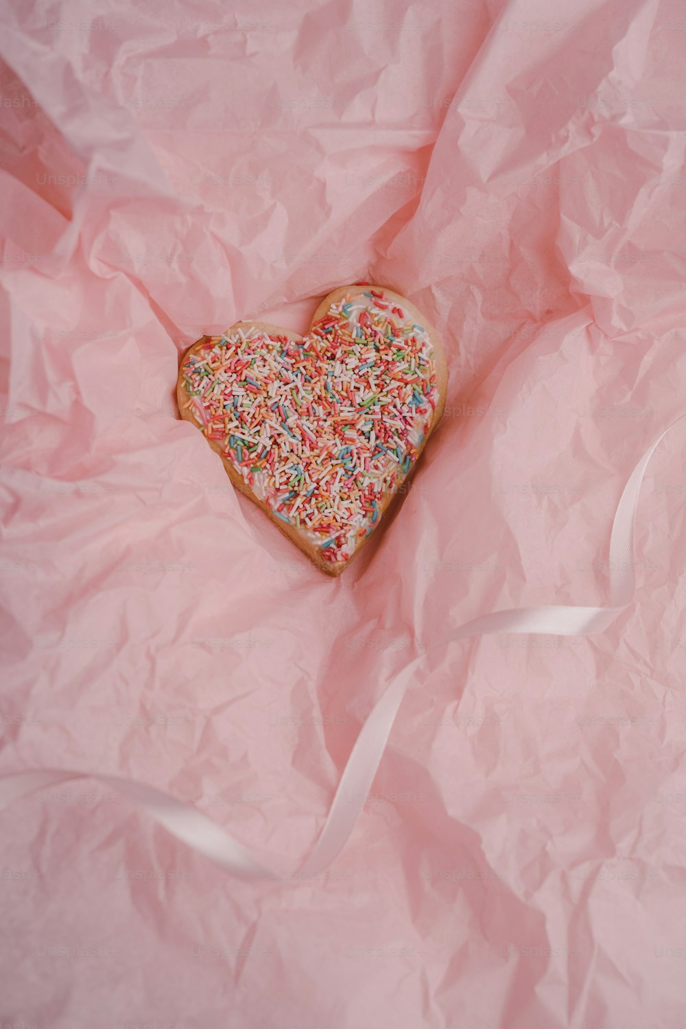Una galleta en forma de corazón con chispas sobre un fondo rosa