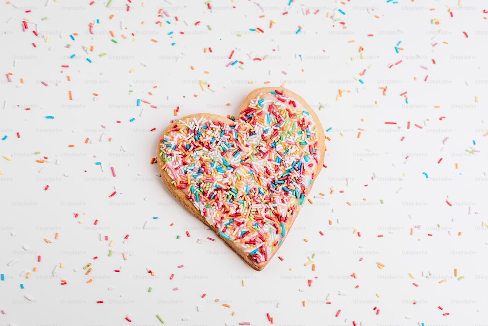 a heart shaped cookie with sprinkles on a white surface
