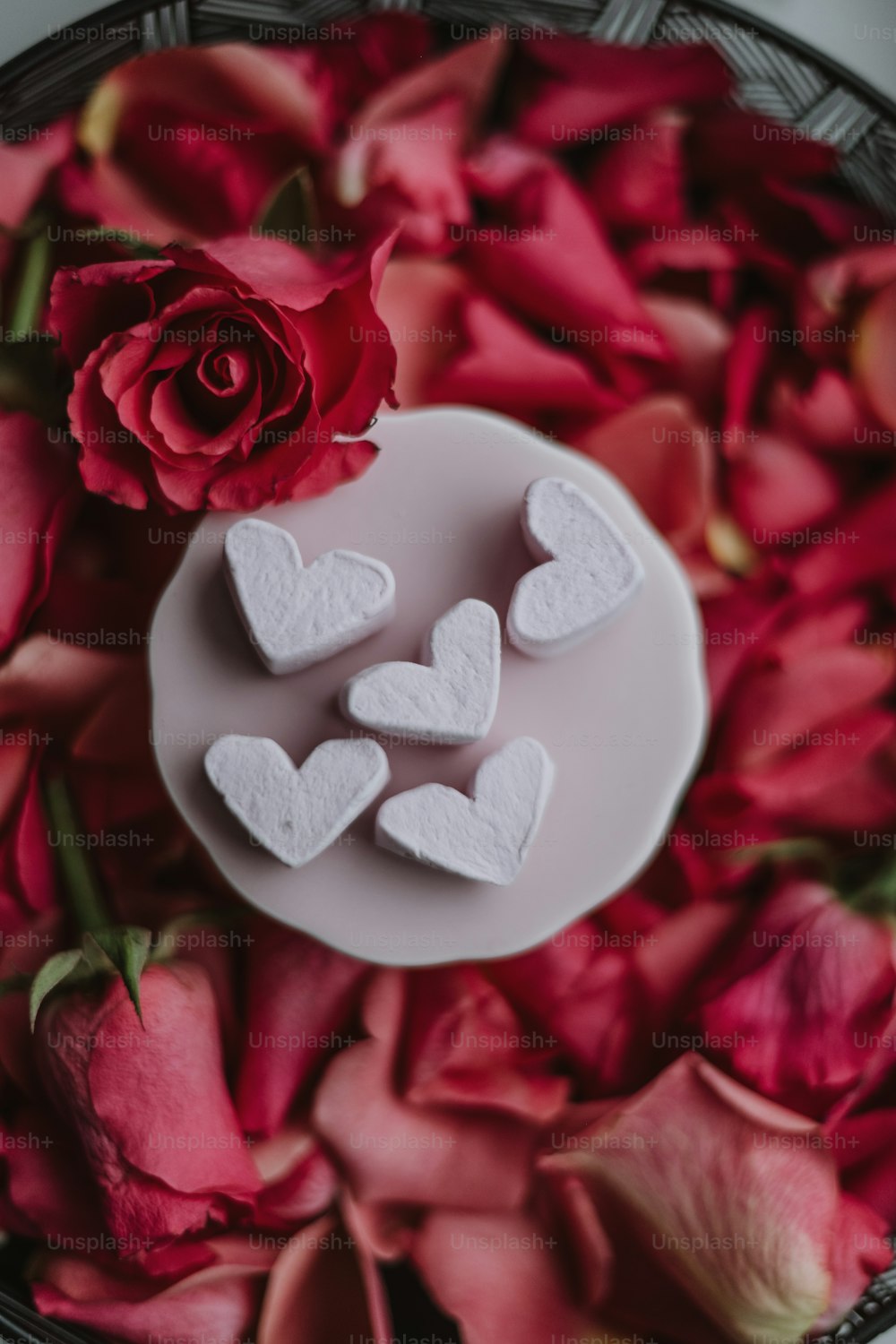 um prato de marshmallows em forma de coração ao lado de uma rosa