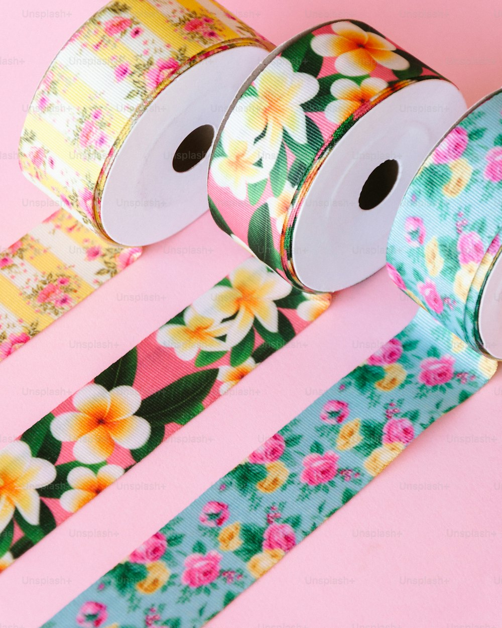 three rolls of colorful floral washi tape on a pink background