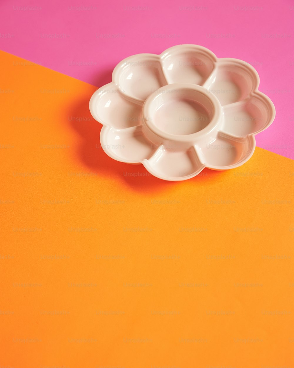 uma tigela branca em forma de flor sentada em cima de uma mesa laranja e rosa