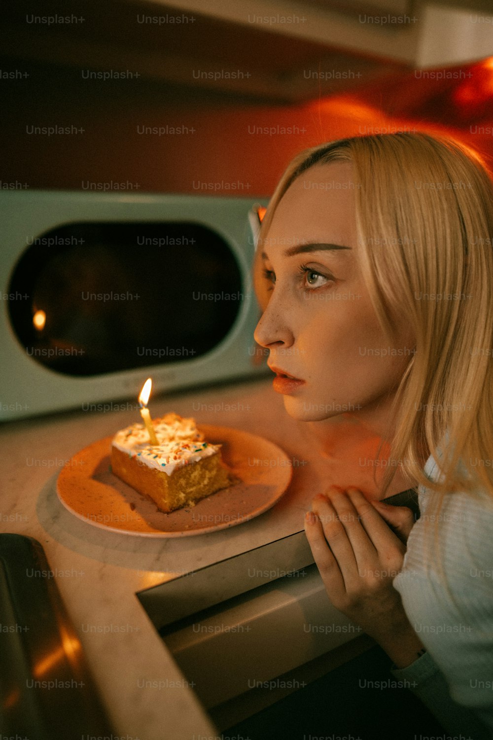 una donna che guarda un pezzo di torta con una candela su di esso