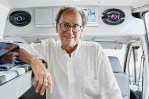 a man in a white shirt and glasses sitting on a bed