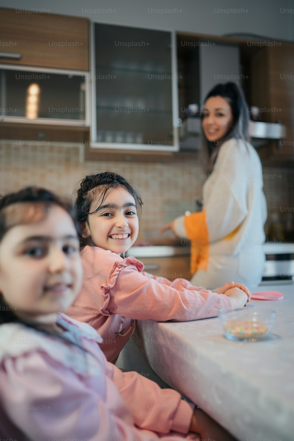 two young girls sitting at a table with a woman in the background