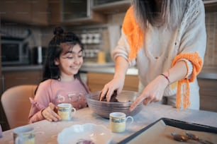 a woman helping a little girl make a chocolate cake