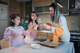 a woman standing next to two girls in a kitchen