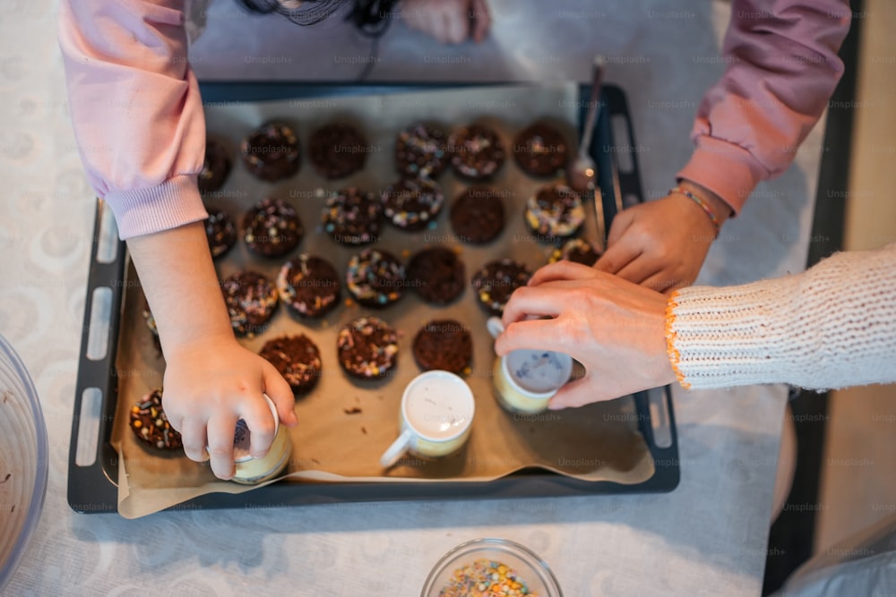 a couple of people standing over a tray of doughnuts