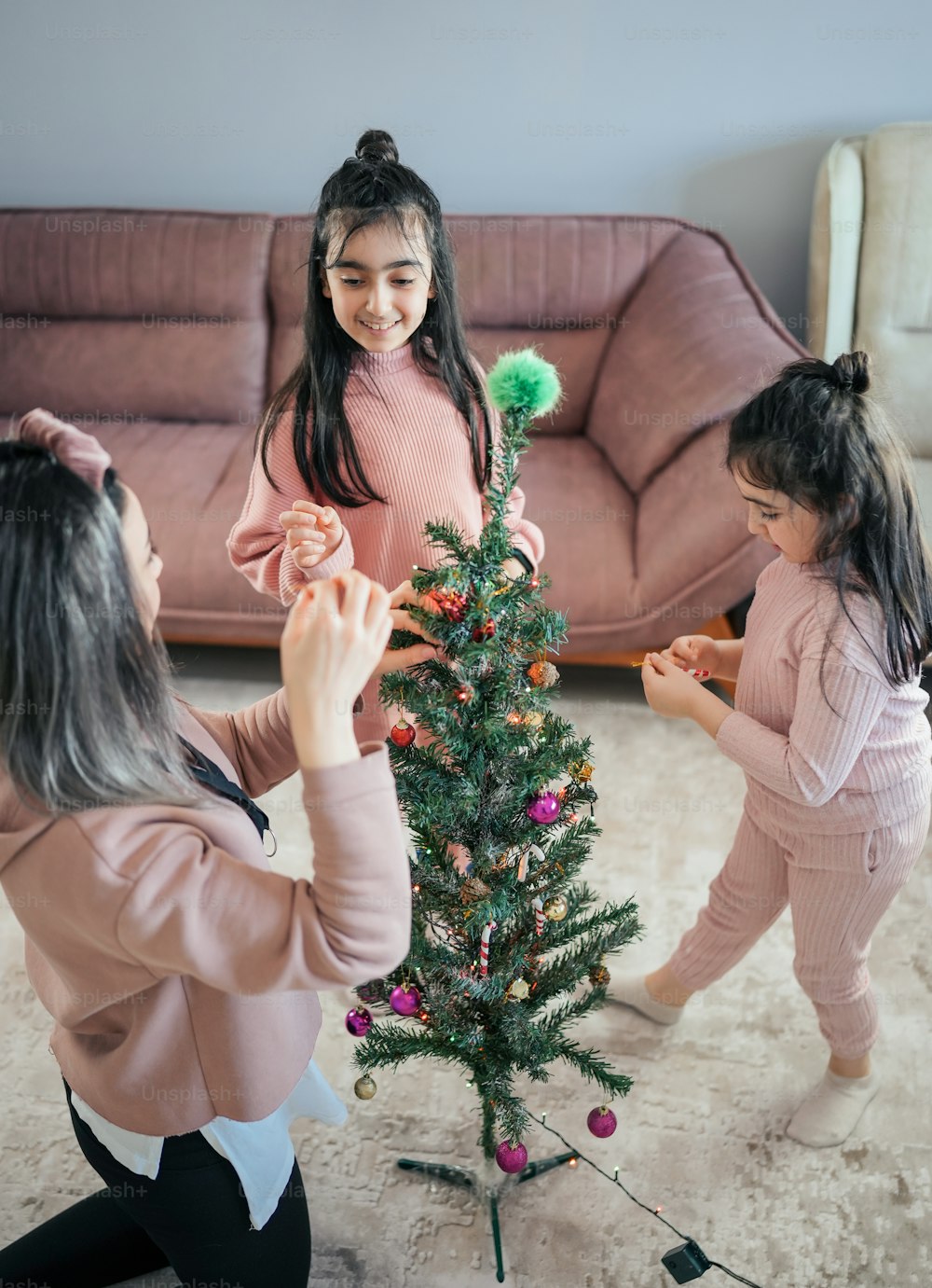 Una mujer y dos niñas decorando un árbol de Navidad