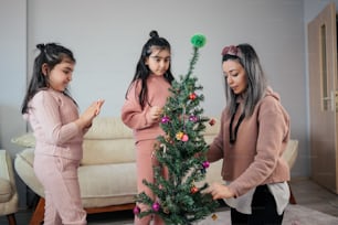 três meninas que decoram uma árvore de Natal em uma sala de estar
