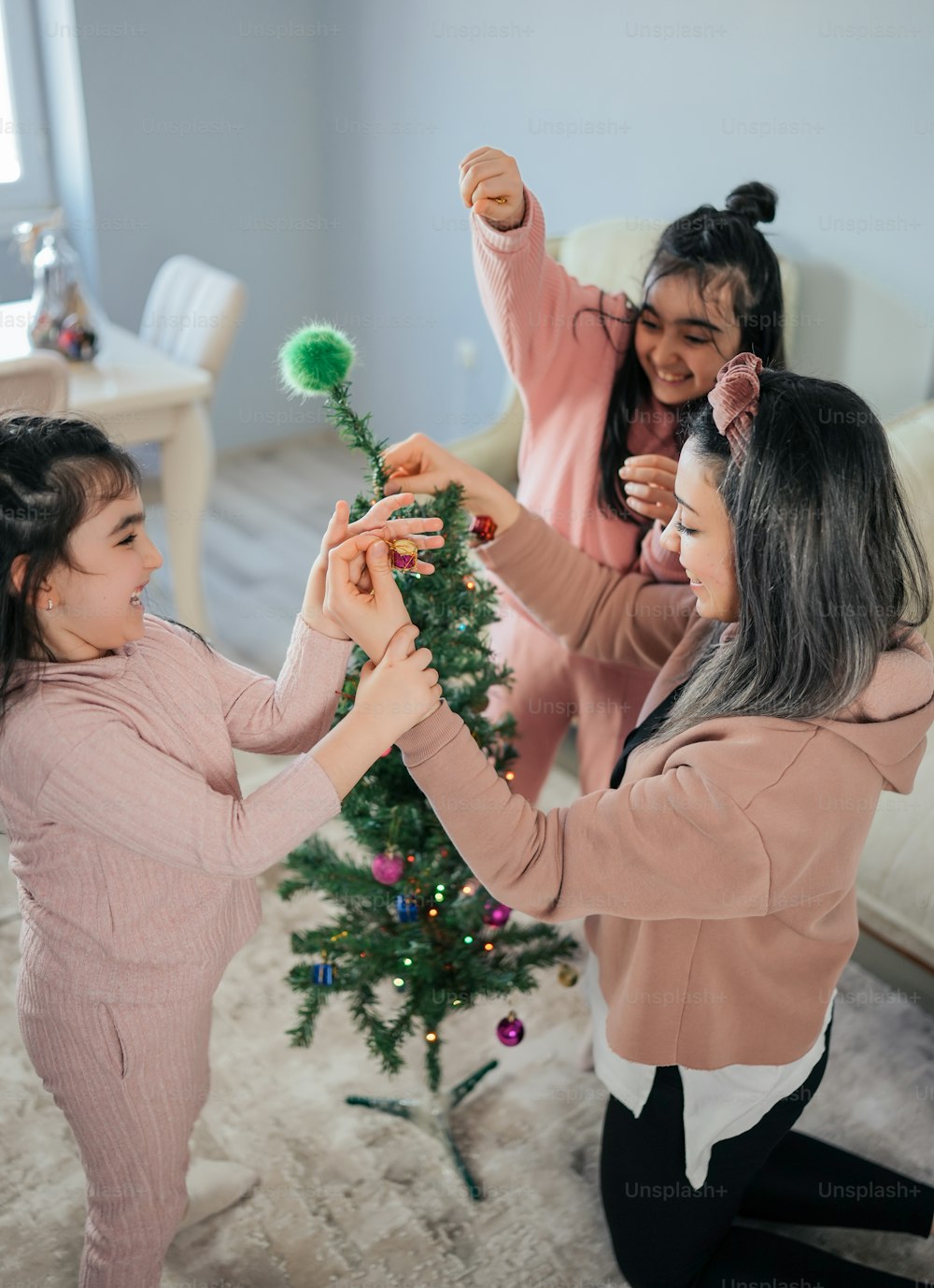 a woman and two girls decorating a christmas tree