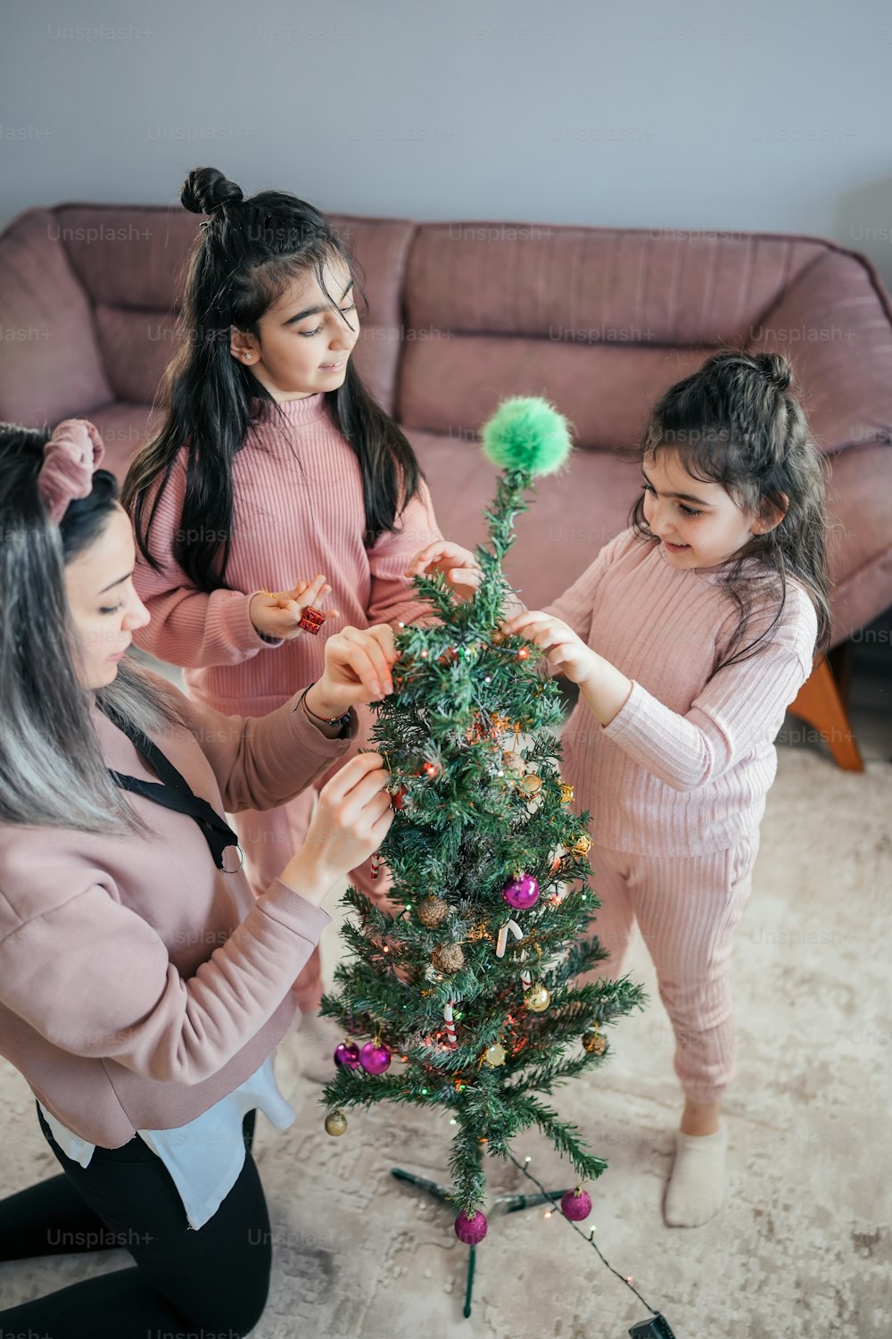 a woman and two girls decorating a christmas tree