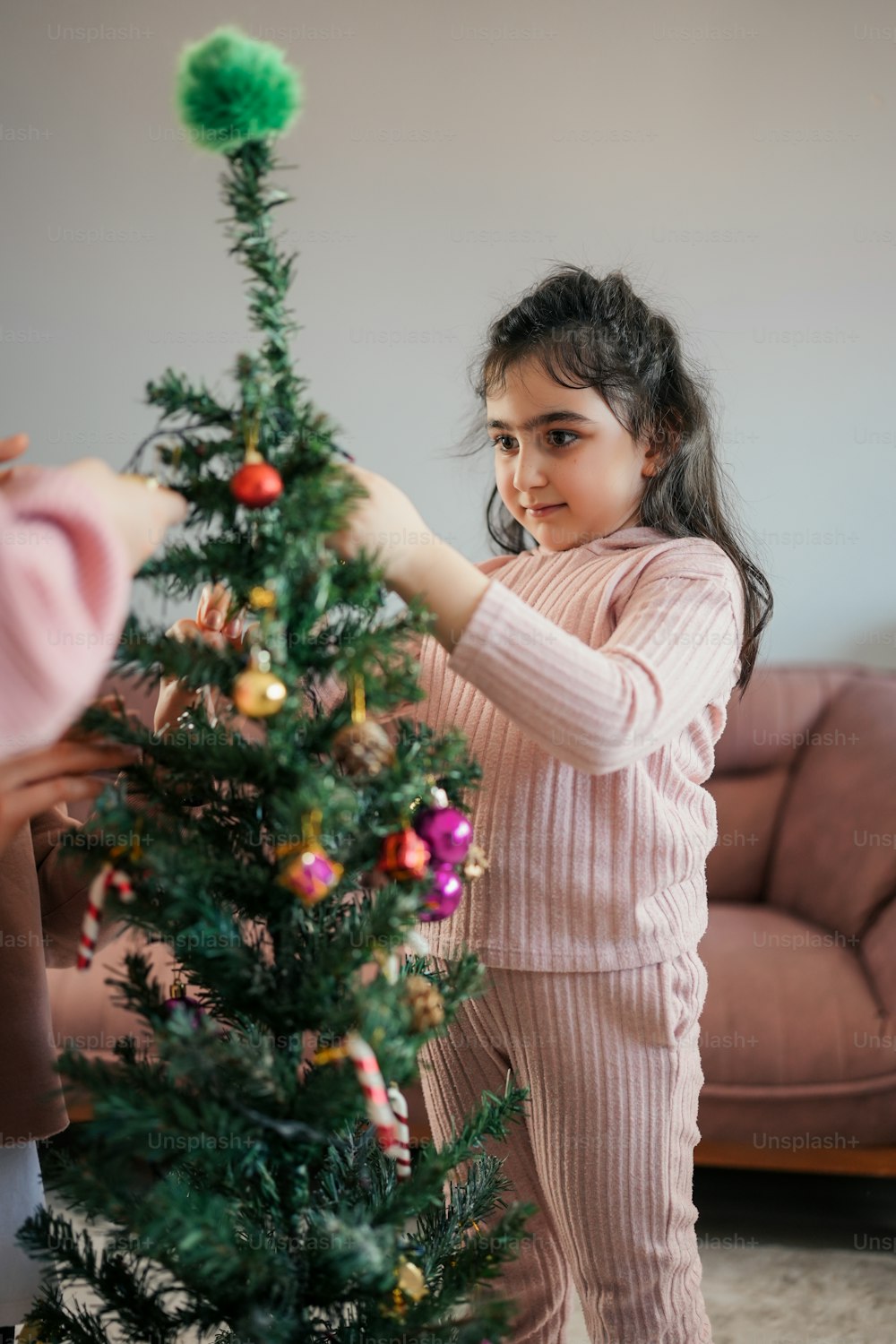 uma menina colocando decorações em uma árvore de Natal