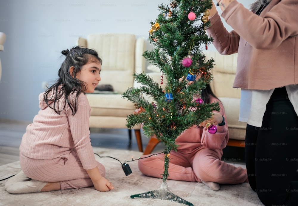 uma menina sentada no chão ao lado de uma árvore de Natal