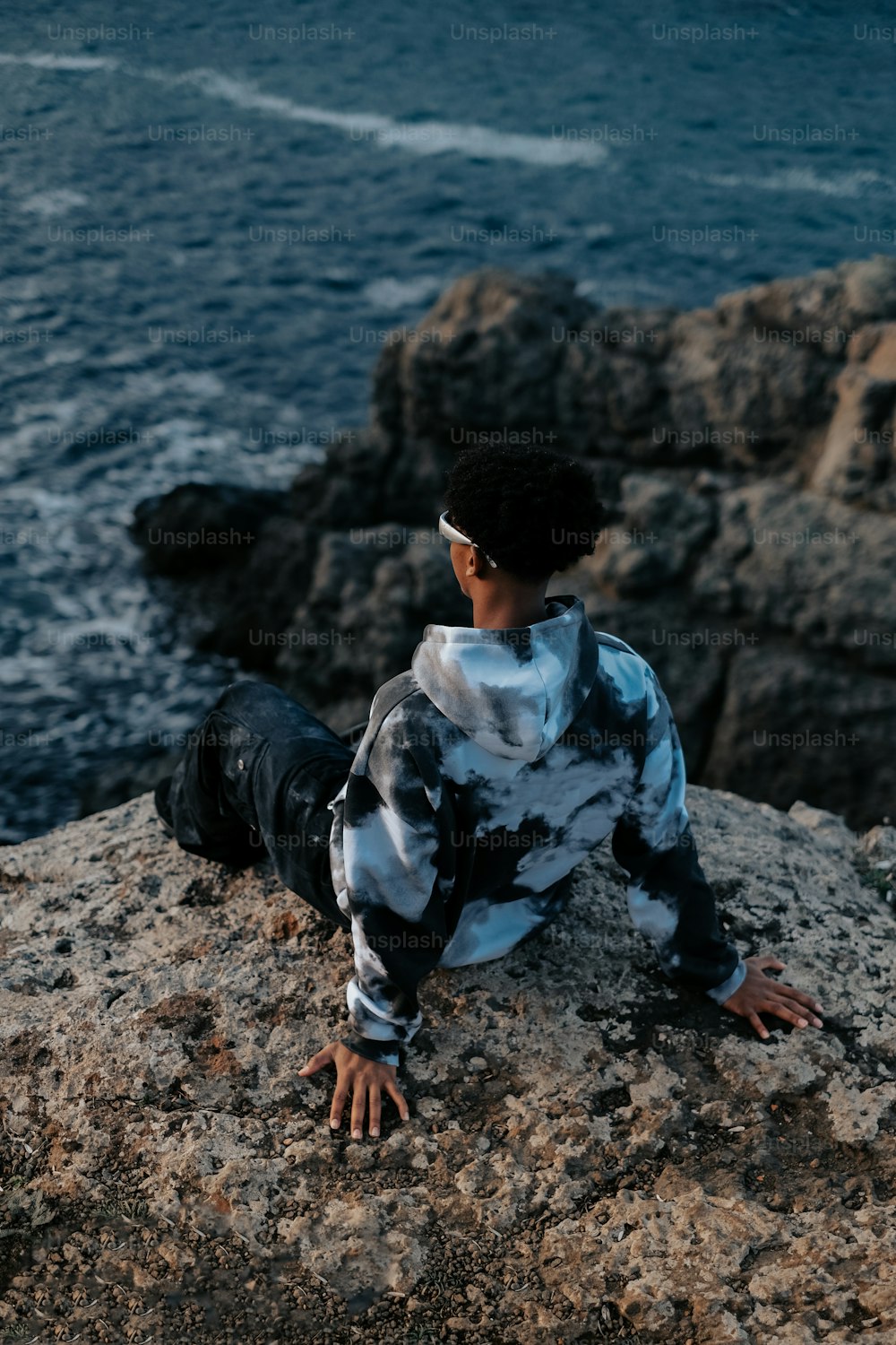a boy sitting on a rock near the ocean